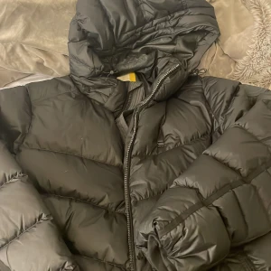 Svart dunjacka från G-Star Raw XXL - Svart dunjacka från G-Star Raw i storlek XXL. Jackan har huva, dragkedja och tryckknappar framtill. Den är quiltad och har en puffig look som är perfekt när det är kallt ute. Materialet är dunfyllt och yttermaterialet känns som syntet.