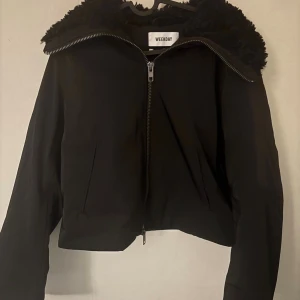 Svart teddyjacka från Weekday - Svart teddyjacka från Weekday med fluffig krage och hel dragkedja framtill. Jackan har en croppad passform och långa ärmar, perfekt för dig som gillar en cool och enkel stil. Materialet är mjukt och syntetiskt med teddy-detaljer på kragen.