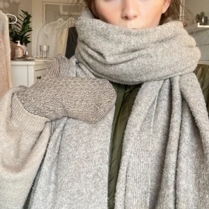 Beige stickad halsduk i ullmix - Säljer en stor och mysig beige halsduk i stickad ullmix. Halsduken är rektangulär och har en enkel, klassisk design utan mönster. Perfekt att svepa flera varv runt halsen för extra värme under kalla dagar. Färgen är neutral och passar till det mesta.