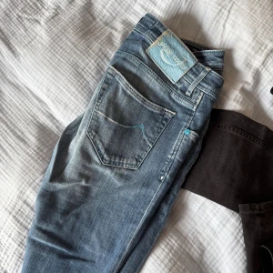 Blå jeans från Jacob Cohen, storlek 32 - Snygga blå jeans från Jacob Cohen i storlek 32. Jeansen har en klassisk femficksdesign, coola blå detaljer vid knappar och sömmar samt ett unikt mönstrat innerfoder med bilar. Materialet är mjukt jeans och passformen är normal med rak siluett.
