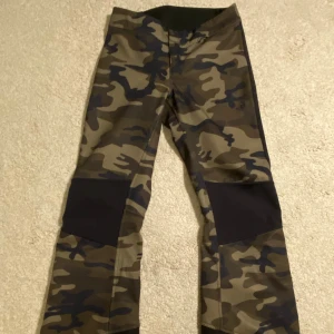 Lågmidjade Täckbyxor Peak Performance  - Säljer ett par täckbyxor från Peak Performance i storlek XS med camouflage-mönster i grönt och svart. Kommer inte till användning då de är för små. Täckbyxorna har en liten ficka fram och dragkedja längs ner på båda benen. Kom privat för fler frågor 💕