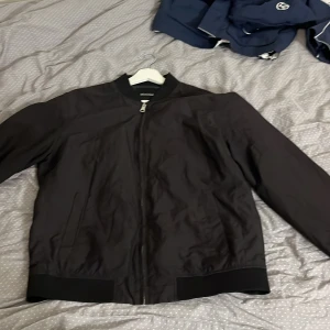 Svart bomberjacka från Matinique XL - Svart bomberjacka från Matinique i storlek XL. Men passar även L Jackan har klassisk ribbad krage och muddar, dragkedja framtill och två sidofickor. Insidan är fodrad med mörkblått och olivgrönt tyg. Perfekt för dig som gillar stilren och enkel design. Tveka inte på att fråga eller ge bud 