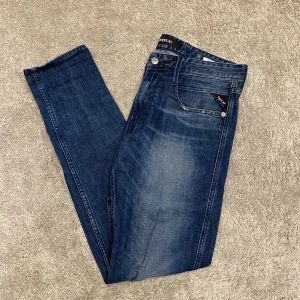 Replay Anbass jeans mörkblå slim - Snygga Replay Anbass jeans i mörkblå tvätt med diskreta slitningar och klassiska fem fickor. Slim passform och normal midja, tillverkade i mjukt jeansmaterial med stretch för extra komfort. Perfekta för dig som gillar stilrena och moderna jeans.