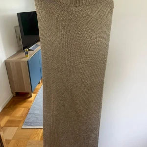 Beige glittrig stickad långkjol - Säljer en beige stickad långkjol med rak passform och elastisk midja. Kjolen har en mjuk och grovstickad struktur som ger en chill och avslappnad vibe. Peeerfekt att dra över bikinin på en beach club!
