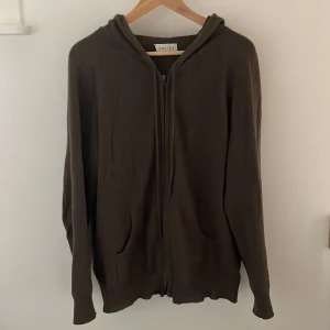 Mörkbrun hoodie från Davida - Säljer en mörkbrun hoodie från Davida Cashmere med dragkedja framtill och två fickor. Tröjan har huva och är långärmad, perfekt för dig som gillar chill och enkel stil. Materialet är kashmir vilket gör den skön att bära under höst och vinter.