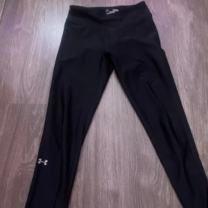 Svarta leggings från Under Armour - Svarta leggings från Under Armour med diskret logga vid vristen. Tight passform och stretchigt material som passar perfekt för träning. Hög midja för extra komfort och stöd. Snygga och funktionella för dig som gillar att röra på dig.