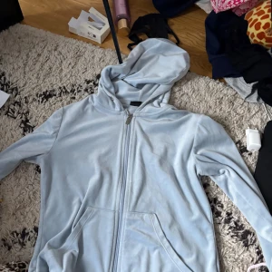 Ljusblå hoodie med dragkedja - Säljer en ljusblå hoodie med dragkedja och huva. Tröjan har två fickor framtill och är tillverkad i mjukt, fleeceliknande material. Perfekt för chill dagar eller när du vill vara extra bekväm. Långärmad och loose passform.