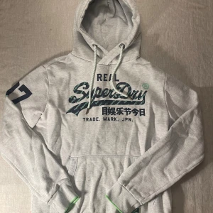 Grå hoodie från Superdry med tryck - | märke: Superdry | plagg: Hoodie | skick: 9/10 | storlek: L passar M | nypris: 1500kr | mitt pris: 349kr | färger: grå | pris kan diskuteras | hör av dig vid minsta fråga eller fundering // LeClosMatteo
