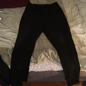 Svarta byxor från Brand Island, L - Svarta byxor från Brand Island i storlek L. De har en rak och enkel siluett med normal passform och midwaist. Materialet känns mjukt och bekvämt, perfekt för dig som gillar stilrena och klassiska plagg.