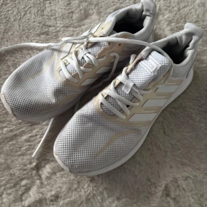 Vita mesh-sneakers från Adidas - Fräscha vita sneakers från Adidas med klassiska tre ränder på sidan och mesh-överdel för extra ventilation. Skorna har snörning och platt sula, samt detaljer i beige. Perfekta för dig som gillar sportig stil och vill ha bekväma skor till träning eller vardag.