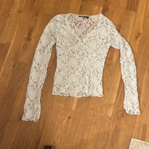 Vit spetsblus med v-ringning - Säljer en vit långärmad blus i spets med v-ringad hals. Blusen har ett romantiskt blommigt spetsmönster och är figurnära i modellen. Perfekt för dig som gillar detaljer och vill ha en feminin look.