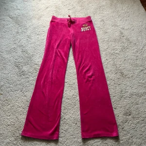 Rosa juicy couture byxor - Supersnygga juicy couture byxor! Byxorna har utsvängda ben, paljettdetalj på framsidan samt knappar på bakfickorna❣️Storlek XS, passar även S. Finns en liten fläck som jag inte märkte förrän jag tog bilderna. Går säkert bort i tvätten!