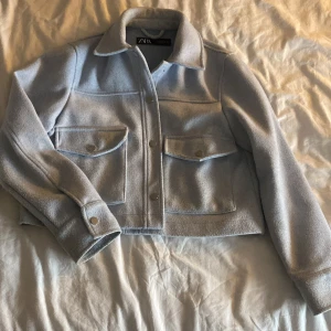 Ljusblå kappa från Zara - Säljer en ljusblå kappa från Zara i storlek S. Jackan har två stora fickor med knappar framtill, klassisk krage och långa ärmar med knappdetaljer vid mudden. Materialet är mjukt och känns som ull, perfekt för lager-på-lager. Enkel och clean look. Endast använt vid 3 tillfällen, därför säljer jag:)