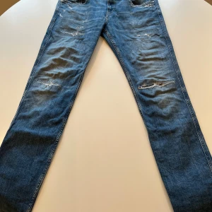 Replay Anbass blå jeans med slitningar - Snygga blå jeans från Replay, modell Anbass, med coola slitningar och detaljer på både fram- och bakfickor. Klassisk femficksdesign, normal passform och raka ben. Perfekt för dig som gillar en avslappnad streetstil. Grymma jeans köpte på nk för något årsedan 100% äkta! Hör av dig vid minsta fundering ha en fin dag! MVH Leo