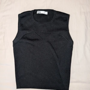 Svart stickad croptop från Zara - Svart stickad croptop från Zara med rund halsringning och cool detaljsöm över bröstet. Toppen är ärmlös och har en enkel, stilren design. Katt finns i hemmet. 