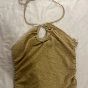 Glittrig guldig halterneck topp - Säljer en glittrig beige tubtopp med halterneck och snygg knytning i nacken. Materialet är mjukt och skimrande, perfekt för när man vill klä upp sig✨🪩Man kan även knyta toppen på olika sätt(se bilder)🥰Pris kan diskuteras!❤️