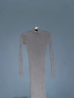 Ljusgrå ribbad långklänning H&M - Supersnygg långklänning från H&M i ljusgrått ribbat material. Klänningen har lång ärm och hög hals, vilket ger en clean och stilren look. Perfekt för dig som gillar minimalistisk stil och vill ha något bekvämt men ändå trendigt.