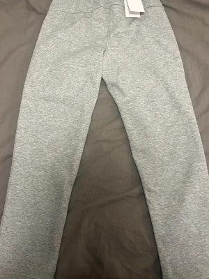 Grå mjukisbyxor från Nike M - Snygga ljusgrå mjukisbyxor från Nike med dragsko i midjan och klassisk logga på benet. Tillverkade i mjukt bomullsmaterial för maximal komfort. Perfekta för chill eller träning. Fickor på sidorna och elastisk midja för skön passform.