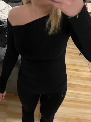 Svart oneshoulder topp från BikBok - Säljer en svart, tight och stilren oneshoulder topp från BikBok. Toppen har lång ärm på ena sidan och är axelbandslös på andra, vilket ger en snygg asymmetrisk look. Materialet är stretchigt och följsamt, perfekt att styla med jeans eller kjol.