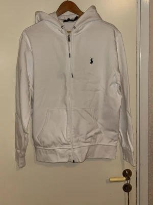 Polo Ralph lauren vit hoddie  - Vit Polo Ralph Lauren hoodie i storlek M. Mycket bra skick, sparsamt använd och väl omhändertagen. Klassisk och tidlös modell med broderad Polo-logga på bröstet.  Nypris: ca 2 100 kr. Inga fläckar, hål eller slitage.