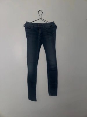 Mörkblå jeans från Replay  - Säljer ett par mörkblå skinny jeans med låg midja. Jeansen har klassisk femficksdesign, smala ben och snygga slitningar framtill. Tillverkade i stretchigt jeansmaterial för en bekväm passform. Perfekta till sneakers eller boots.