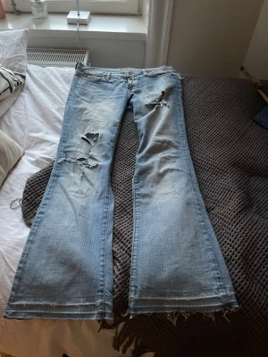Lågmidjade bootcut jeans med hål - Jätte jätte snygga och coola jeans med skor snygga slitningar vid benen. De har en liten defekt som man ej tänker på vid sista bilden. Midjemåttet- 39 cm. Innerbenslängden- 77 cm. Första bilden är med lampan i rummet av, andra bilden är med den på så man ser i olika ljus. 