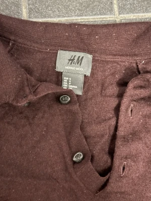 Brun merinoull pikétröja H&M - Mysig mörkbrun pikétröja från H&M i mjuk merinoull. Tröjan har klassisk krage, knappar framtill och långa ärmar. Perfekt för dig som gillar stilrena och bekväma plagg med en enkel men snygg look. Dock är den lite nopprig men är i acceptabelt skick. Kan gå ner i pris ordentligt vid snabb affär! 