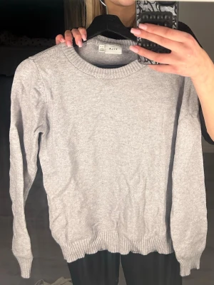 Ljusgrå stickad tröja från Vila - En enkel och stilren ljusgrå stickad tröja från Vila. Tröjan har rund halsringning, ribbade muddar vid ärmslut och nederkant samt lång ärm. Perfekt basplagg till garderoben och lätt att matcha med allt.