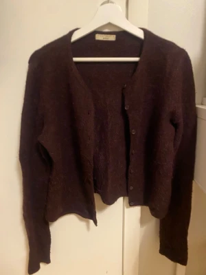 Stickad kofta från Gina tricot  - Mysig burgundy kofta från Gina tricot med lång ärm och sopiga knappar framtill pe Hi. Koftan är gjord i en fluffig ullmix normal insvängd passform. Perfekt för lager på lager under höst och vinter.