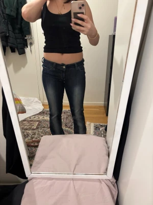 Blå bootcut jeans från Cheap Monday - Säljer ett par mörkblå bootcut jeans från Cheap Monday med snygga slitningar och klassiska gula sömmar. Jeansen har låg midja och är tillverkade i bomull. Perfekta om du gillar en retro vibe och vill ha ett par jeans som sticker ut lite extra.