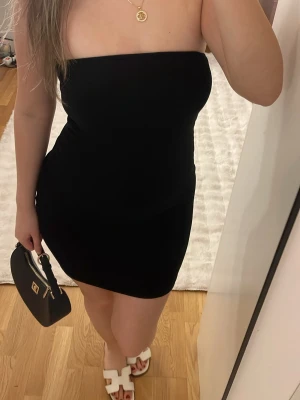 Svart axelbandslös kortklänning från Zara - Säljer en svart, tight och axelbandslös kortklänning med enkel och stilren design. Klänningen har en figurnära passform och är perfekt för dig som gillar minimalistisk stil. Materialet känns mjukt och stretchigt, vilket gör den bekväm att bära.