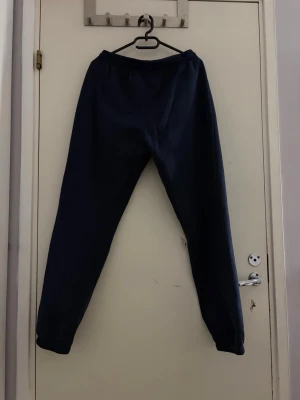 Mörkblå mjukisbyxor med resår - Mörkblå mjukisbyxor med resår i midjan och bensluten. Byxorna har snörning i midjan och sidofickor. Perfekta för chill dagar eller när du vill vara bekväm. Tillverkade i mjukt bomullsmaterial.