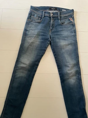 Replay Anbass hyperflex herr - Säljer ett par Replay Anbass jeans i klassisk blå tvätt med snygga slitningar. Modellen har fem fickor, normal midja och smal passform. Jeansen är gjorda i stretchigt bomullsmaterial för extra komfort och har Replay-logga på bakfickan.
