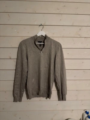 Beige half zip tröja från H&M - Säljer en beige långärmad tröja från H&M i slim fit-modell. Tröjan har en snygg half zip-dragkedja vid halsen och ribbade muddar. Perfekt för dig som gillar stilrena och enkla plagg med en modern touch.