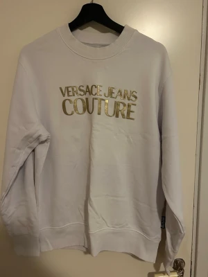 Vit Versace Jeans Couture tröja storlek L-Äkta  - Säljer en helt ny, oanvänd Versace Jeans Couture tröja i storlek L. Tröjan är vit med guldtext på framsidan och är äkta. Den är aldrig använd och är i perfekt skick.
