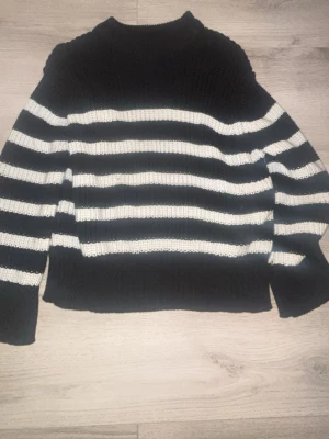 Randig stickad tröja från Gina Tricot - Säljer en svart och vit randig stickad tröja från Gina Tricot. Tröjan har lång ärm, och är ribbstickad för extra mysfaktor. Perfekt för kyliga dagar och enkel att styla med jeans eller kjol. använd en gång 