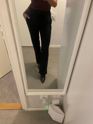 Svarta kostymbyxor med raka ben - Säljer ett par svarta kostymbyxor med hög midja och raka ben. Byxorna har knäppning framtill med flera knappar och sidfickor. Perfekta för en clean och stilren look, passar till både boots och sneakers.