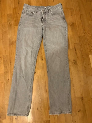 Grå raka jeans med normal passform - Säljer ett par grå jeans med rak siluett och klassisk femficksdesign. Jeansen har normal passform och är tillverkade i jeansmaterial. Färgen är ljusgrå och de har en enkel look utan mönster eller extra detaljer. Perfekta om du gillar stilrena och bekväma jeans.