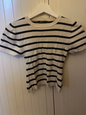 Randig ribbad topp från Gina Tricot - Säljer en kortärmad, croppad topp från Gina Tricot i storlek S. Toppen är vit med svarta horisontella ränder och har en ribbad struktur. Den har rund halsringning och sitter figurnära.💕