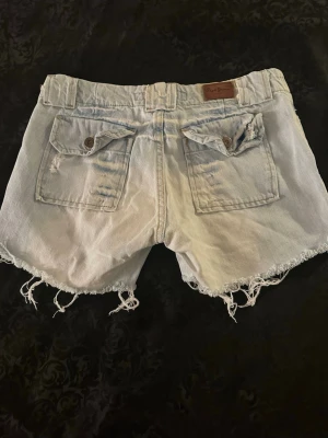 Ljusa denimshorts från Pepe Jeans XS  - Säljer ett par ljusblå denimshorts från Pepe Jeans Piccadilly med fransiga och slitna kanter. Shortsen har två bakfickor med lock och knapp, bälteshällor och klassisk jeansknapp. Perfekta för chill dagar under sommaren.
