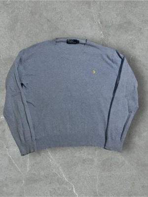 Ljusblå stickad tröja Ralph Lauren | M - Snygg ljusblå stickad tröja från Ralph Lauren med v-ringad hals och klassisk gul logga broderad på bröstet. Tröjan har långa ärmar och ribbade muddar vid ärmslut och nederkant. Väldigt små fläckar kolla bilder.