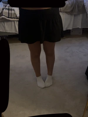 Svart kortkjol från Gina Tricot - Supersöt svart kortkjol från Gina Tricot med smockad midja som ger en skön och flexibel passform. Kjolen har en lätt utställd form och är perfekt för dig som gillar en enkel men snygg stil. Passar till allt och är lätt att matcha. Använd 1 gång.