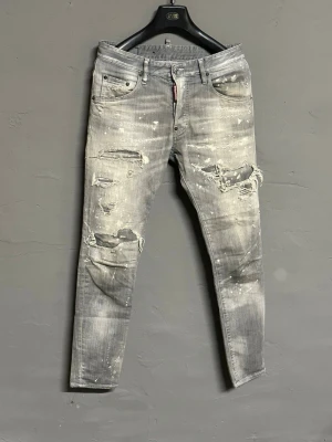 Grå Dsquared2 Skater Jeans, stl 44 - Grå jeans från Dsquared2 i modellen Skater Jean. Byxorna har slitningar, hål och vit färgstänk för en riktigt edgy look. Femficksmodell med låg midja och smal passform. Tillverkade i Italien av bomullsmix.