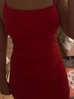 Röd kort klänning från BikBok XS - Säljer en röd figurnära kort klänning från BikBok i storlek XS. Klänningen har tunna axelband, öppen rygg med snörning och är tillverkad i ett stretchigt material. Perfekt för dig som vill ha en enkel men snygg look.
