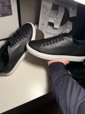 Svarta sneakers från Axel Arigato. orginall pris 2600 - Säljer ett par stilrena svarta sneakers från Axel Arigato med vit platt sula och svart snörning. ALDRIG ANVÄNDA. kommer med box och påse!