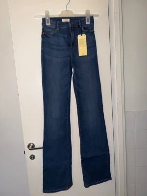 Blå bootcut jeans- Mira från Lindex - Säljer ett par blå Mira 'The curve flare' jeans från Lindex i superstretchigt material. Hög midja och utsvängda ben ger en snygg siluett. Säljer då de är helt nya och oanvända pga köpt fel storlek och kan ej lämna tbx💕