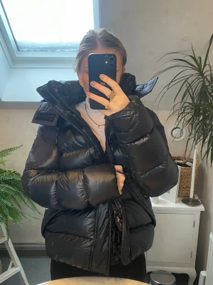 Svart pufferjacka från Colmar - Säljer en svart pufferjacka från Colmar Originals med glansig finish och stor huva. Jackan har tydlig logga på ärmen och insidan är mönstrad med Colmar-tryck. Perfekt för kalla dagar! 