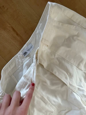 Vita cargobyxor från Zara - Säljer ett par vita cargobyxor från Zara med raka ben och flera fickor på sidorna. Byxorna har normal passform och stängs med dragkedja och knapp. Tillverkade i bomull för en skön och avslappnad look.