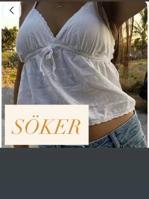 Vit omlott linnetopp med knyt - Superfin vit omlott linnetopp med smala axelband och knyt under bysten. Toppen har en lätt rynkad effekt och spetsdetaljer längs kanterna. Perfekt till jeans eller shorts under varma dagar.