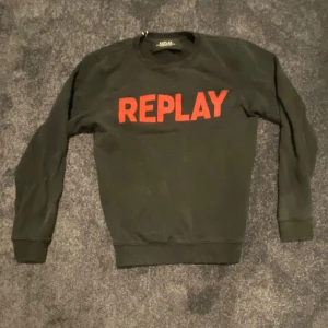 Svart sweatshirt från Replay med röd text - Cool svart sweatshirt från Replay med stor röd REPLAY-text på bröstet. Tröjan har rund hals, långa ärmar och ribbade muddar vid ärmslut och nederkant. Perfekt för dig som gillar streetwear och vill sticka ut med en enkel men snygg design.